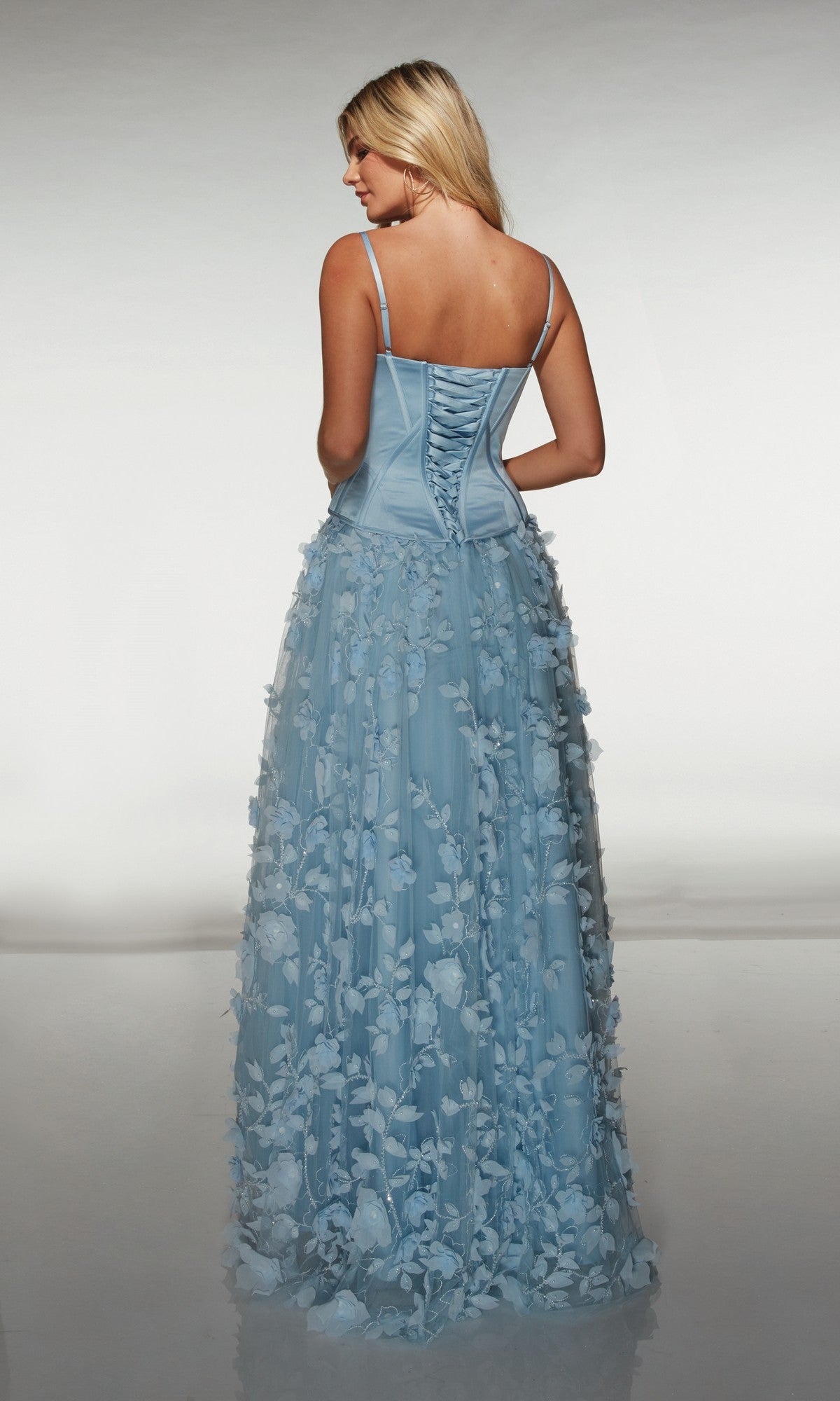 Woman wearing the Alyce 62072, a light blue long formal dress with a corset bodice and 3D floral-lace appliques, stands facing away from the camera.